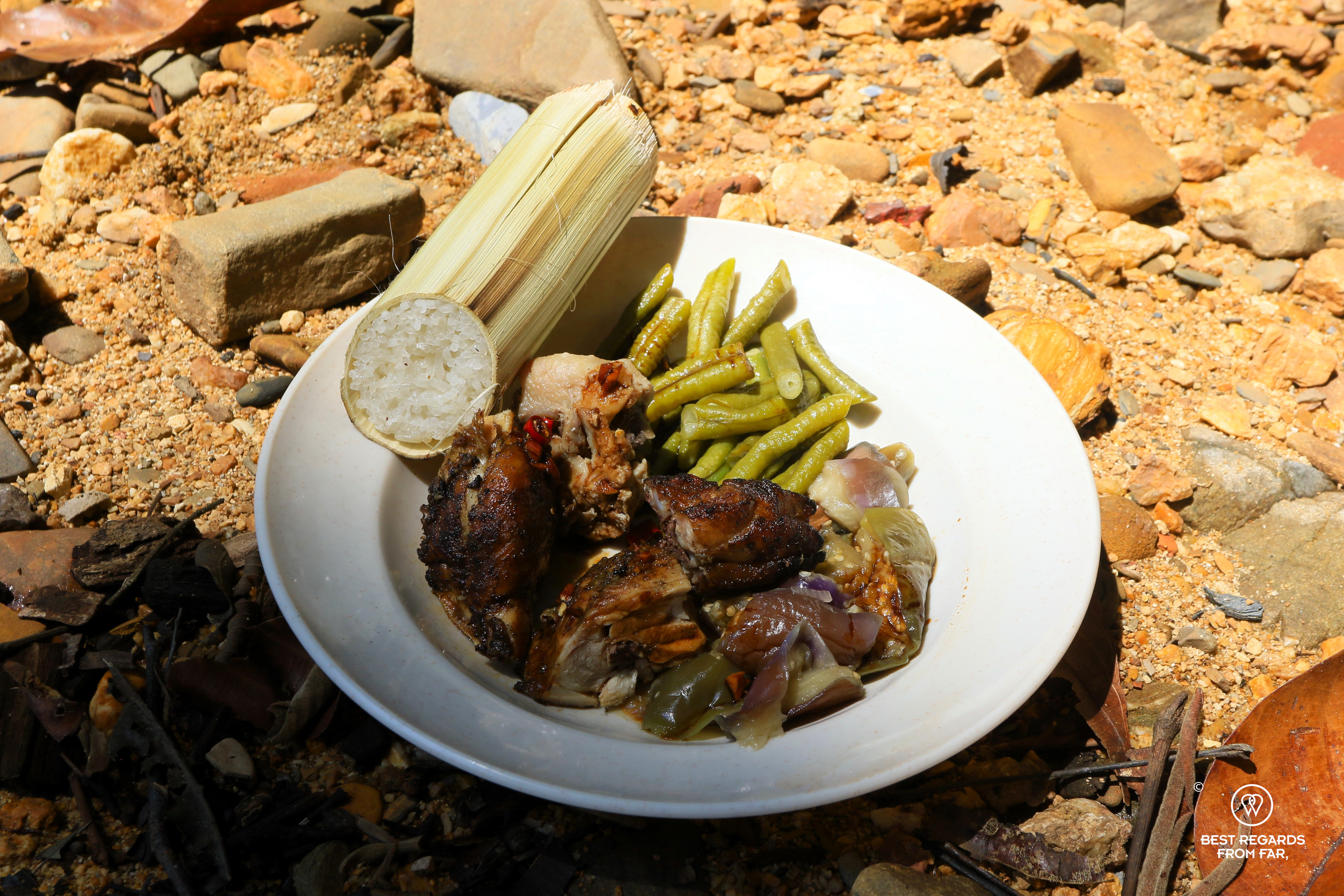 White plate on stones filled with grilled chicken, bamboo sticky rice, green beans and steamed aubergines.