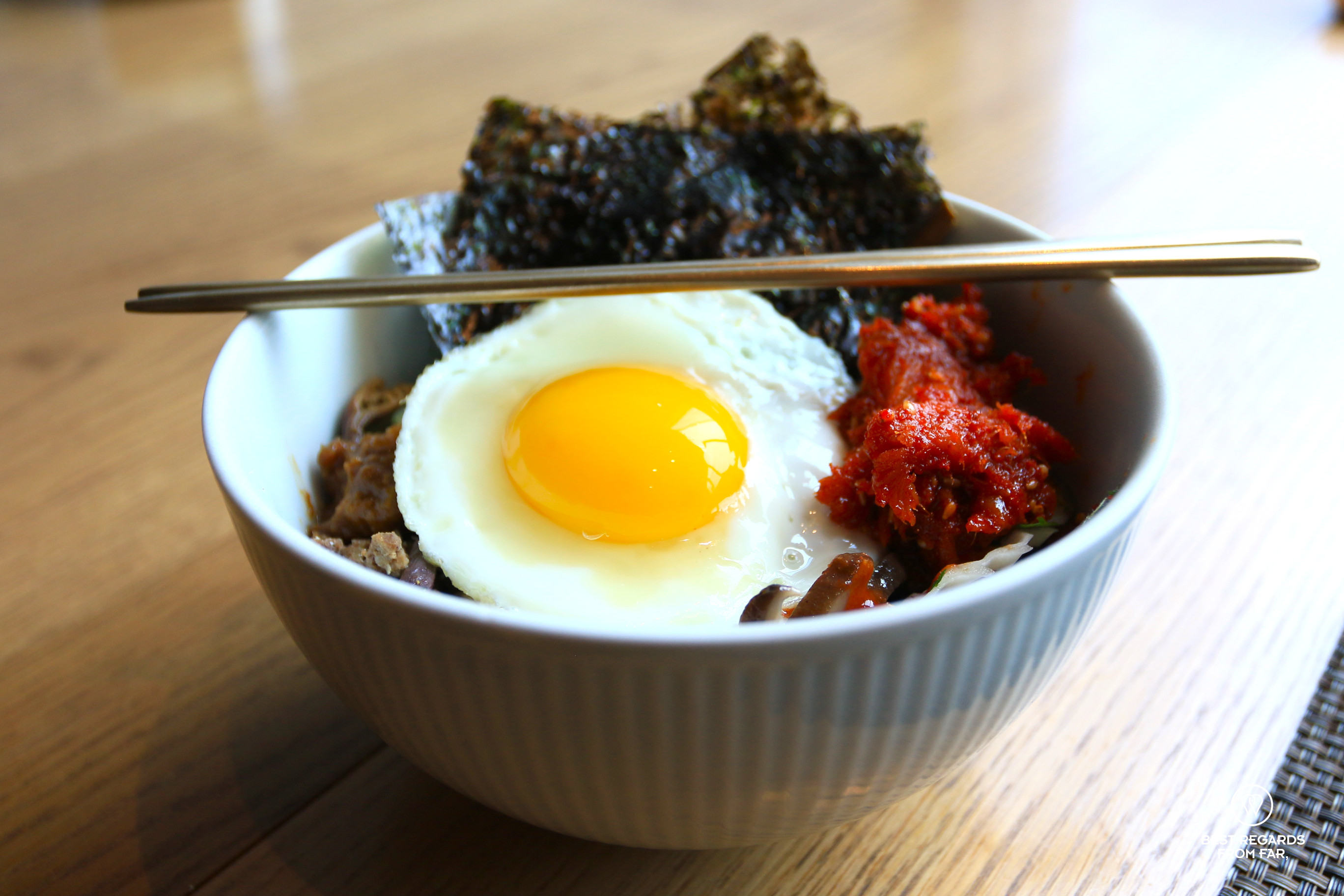 Bibimbap with a fried egg on top and metal chopsticks.