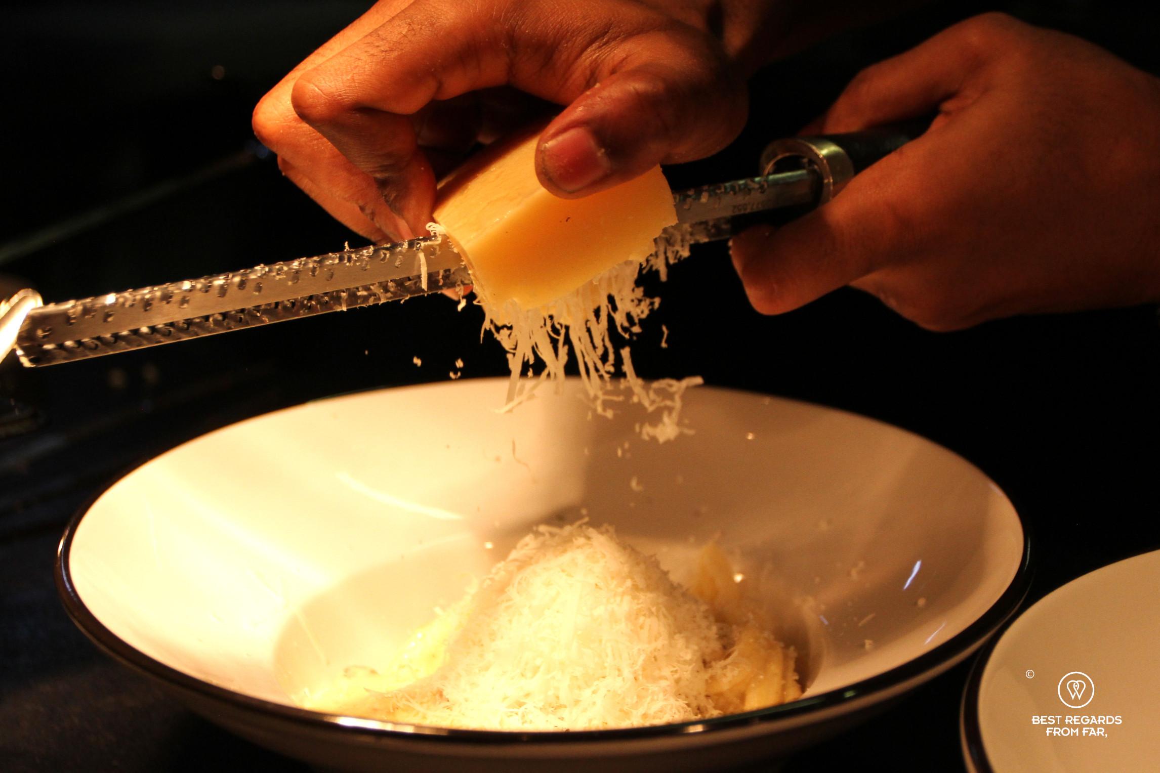 Cook grading parmesan cheese on a pasta dish at Scala Pasta Bar in Cape Town.