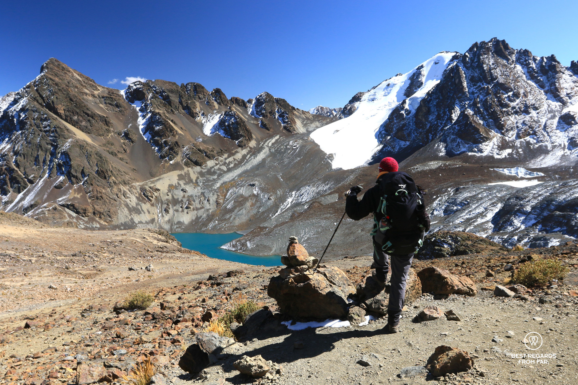 Hiker overlooking a deep blue lake and snow-capped mountains on the way to Pico Austria.