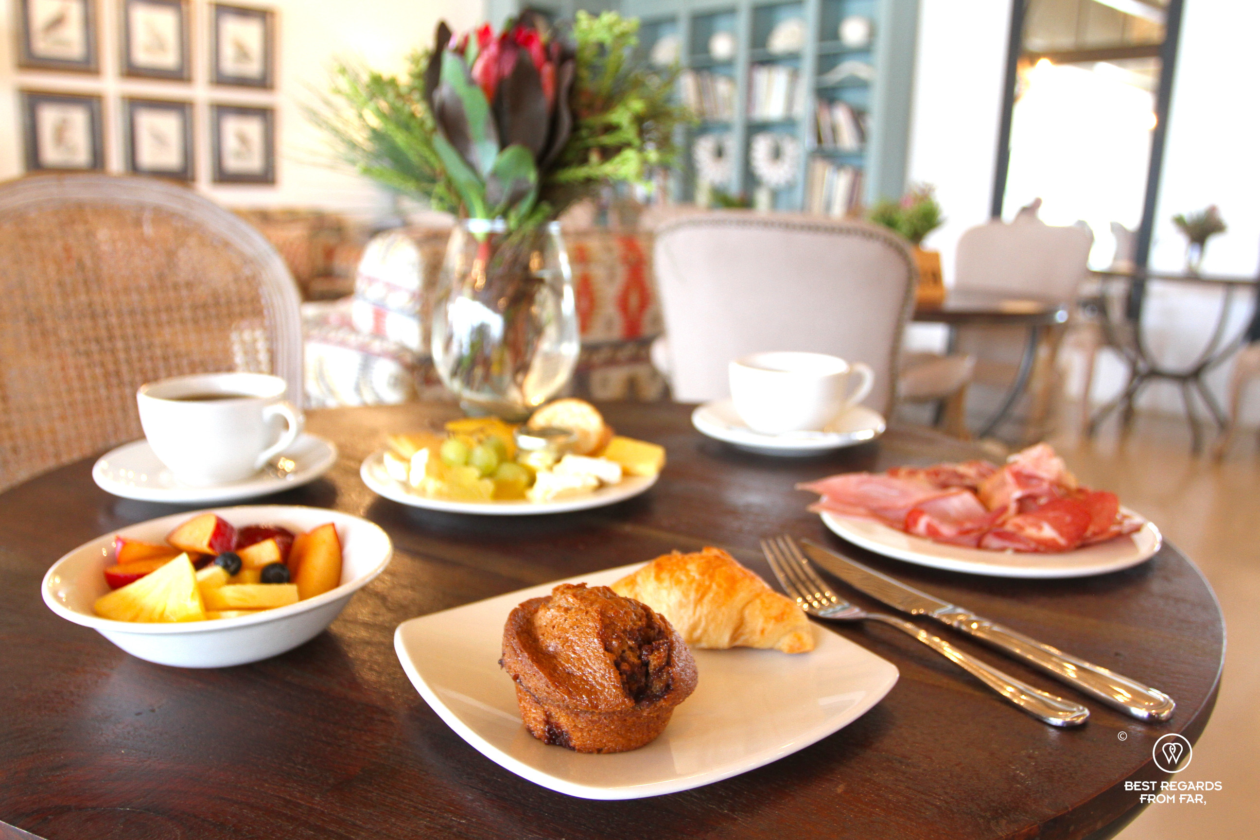 Plates with cold cuts, fresh fruit salad, coffee and a muffin on a wooden table.