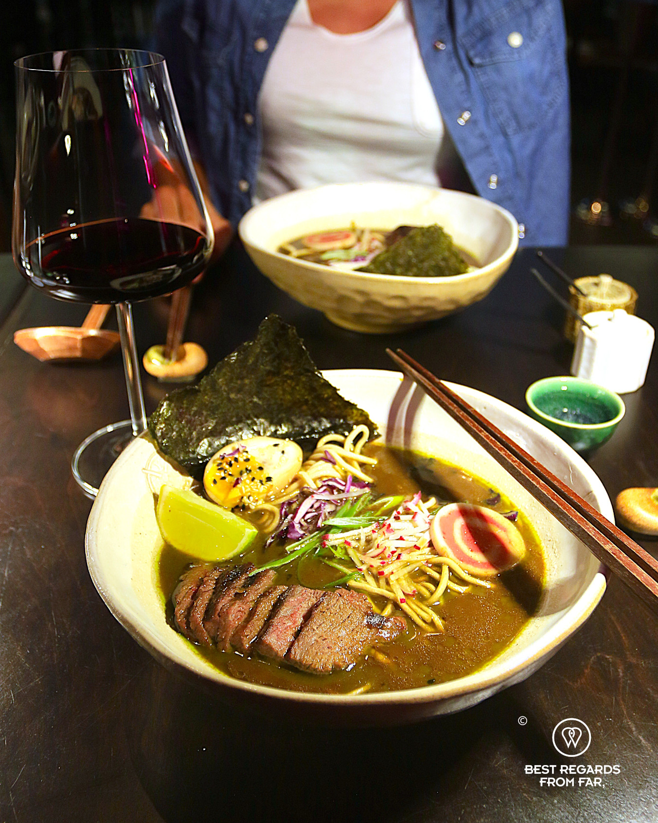 Truffle ramen bowl with steak, egg, and vegetables by a glass of red wine at Yatai ramen bar in Cape Town.