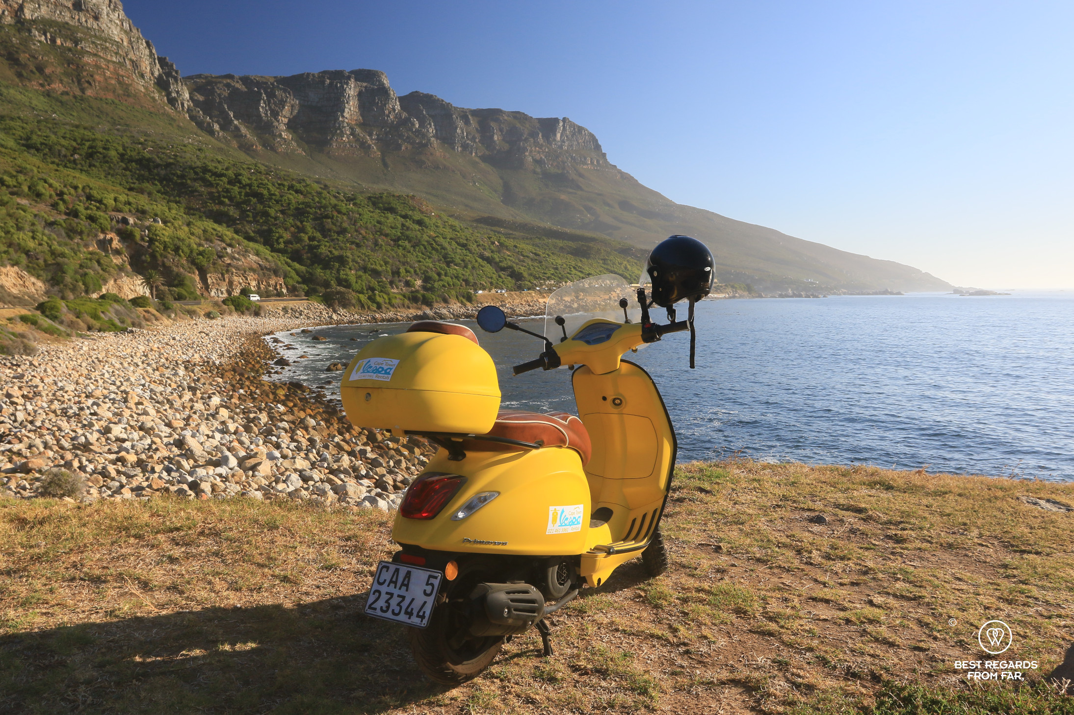 Yellow Vespa scooter parked by the beach in front of the 12 Apostles in Cape Town.