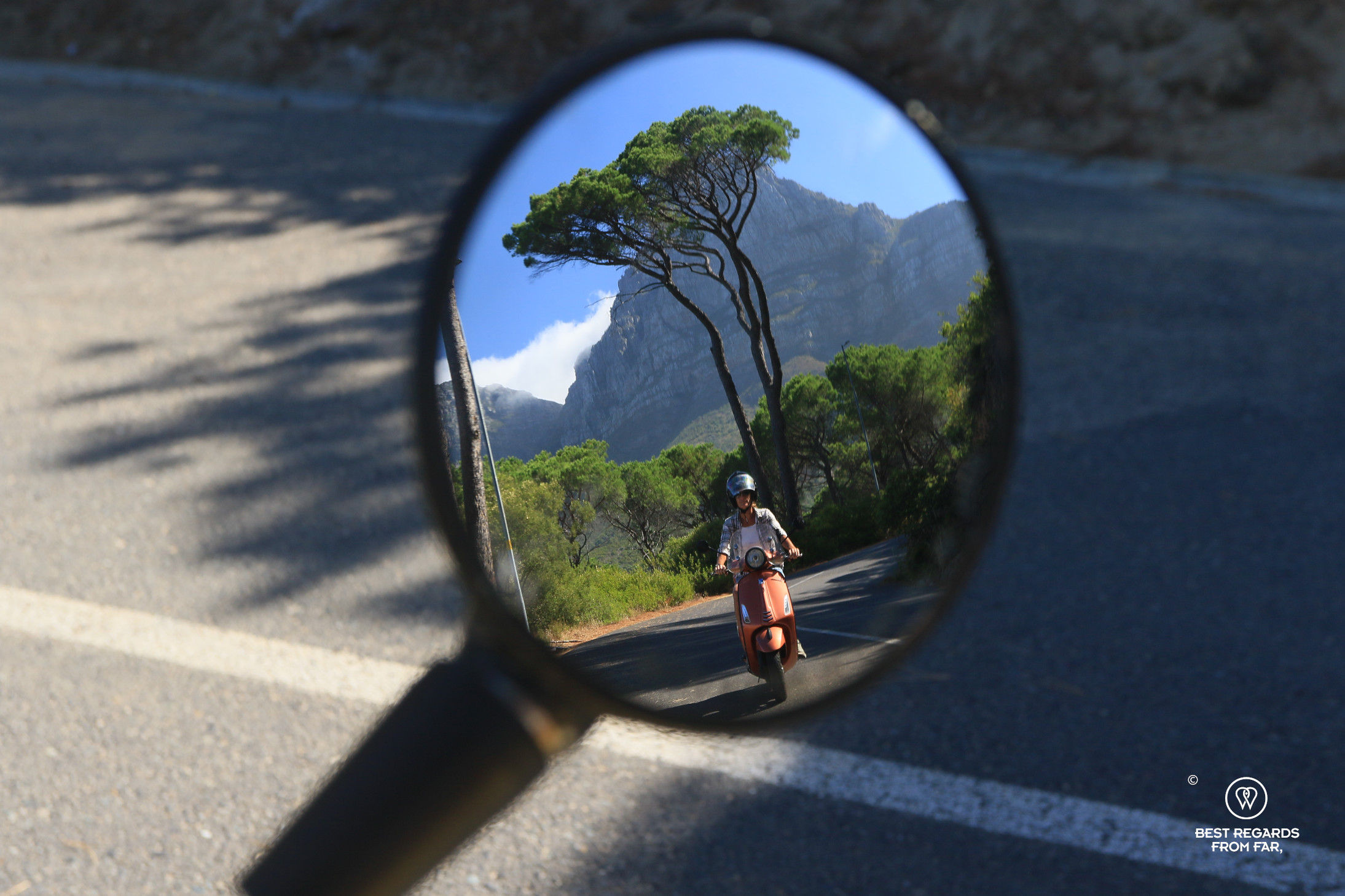 Photo of a Vespa rider taken from a Vespa mirror with Table Mountain in the background.