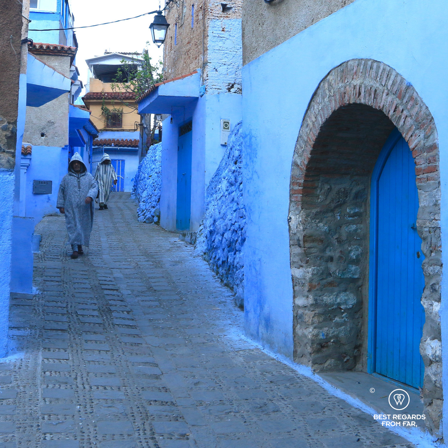 Two Berber men wearing the traditional woolen djellaba of the Rif Mountains in the blue streets of Chefchaouen.