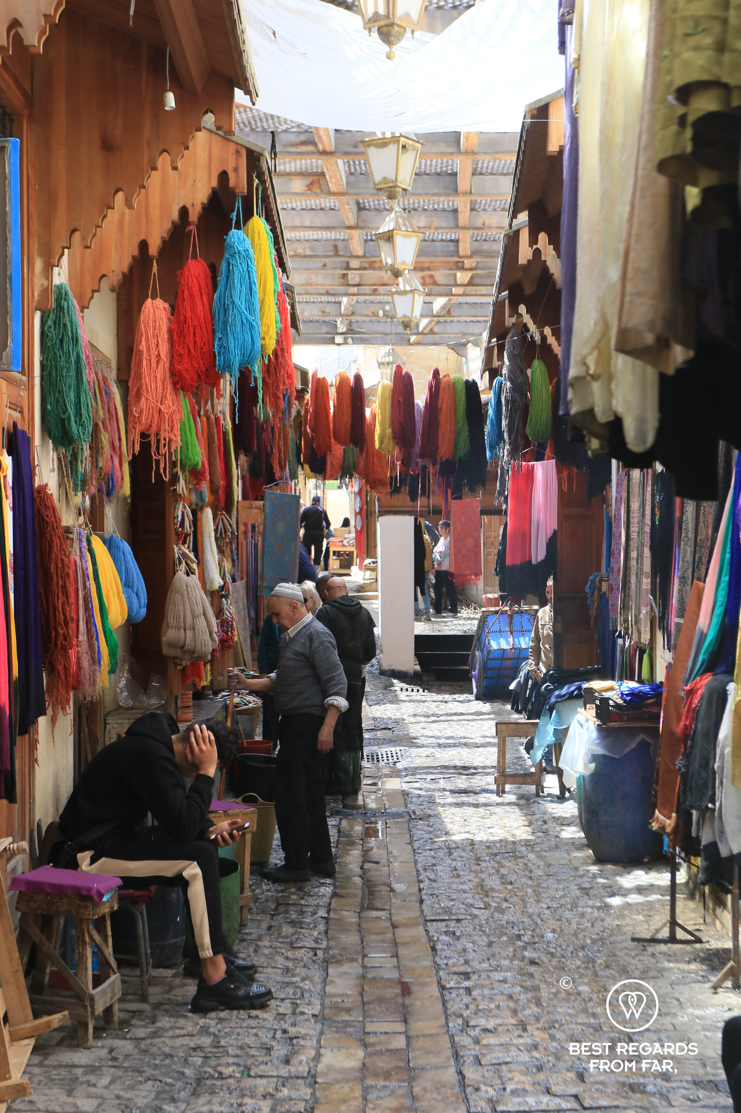 Freshly dyed fabrics drying over a cobblestone street in Fez.