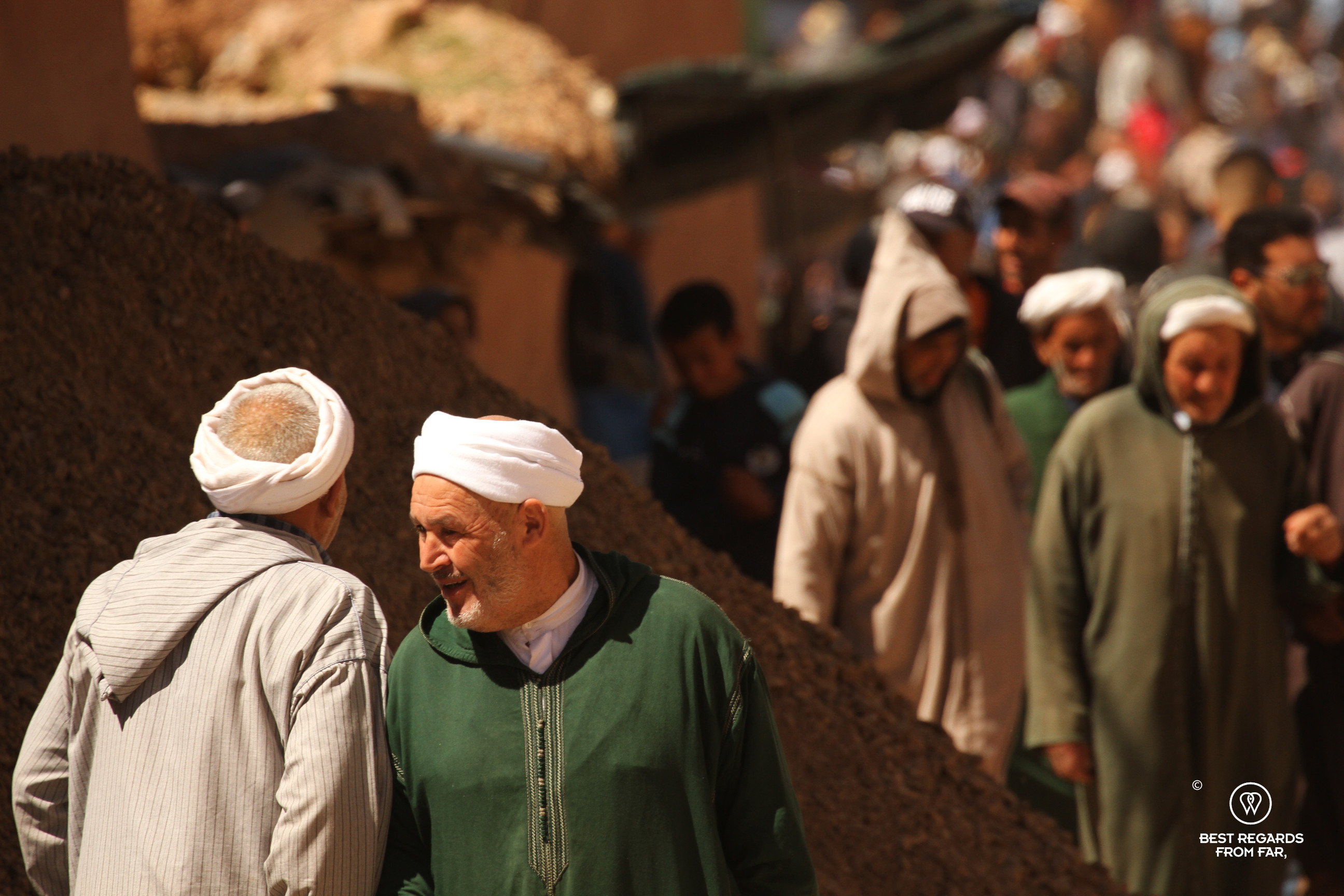 Two men wearing turbans greeting each other on the souk in Morocco.