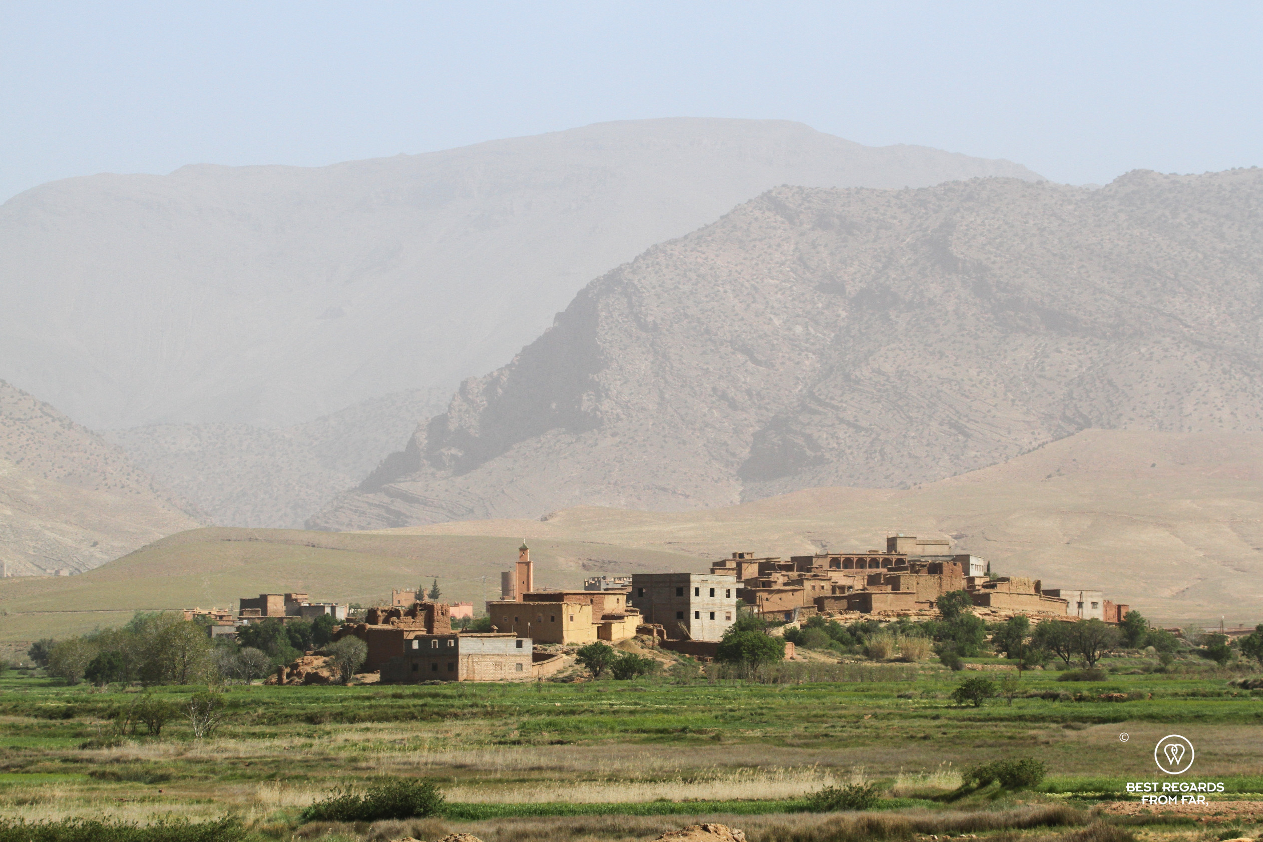 The village of Allemdoun in Morocco with green gardens in the foreground and arid mountains in the background.