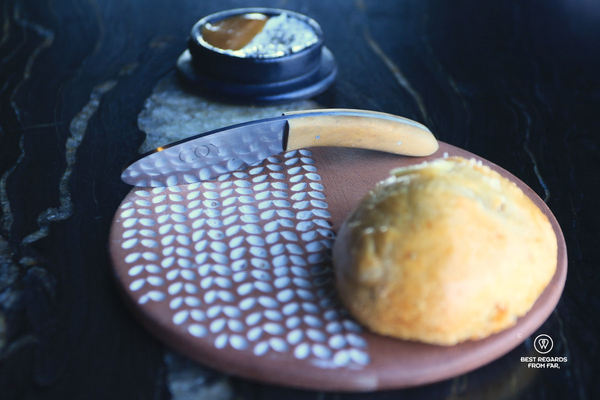 Coy butter knife by a sourdough bread roll on a dark table at the fine dining restaurant Coy in Cape Town.