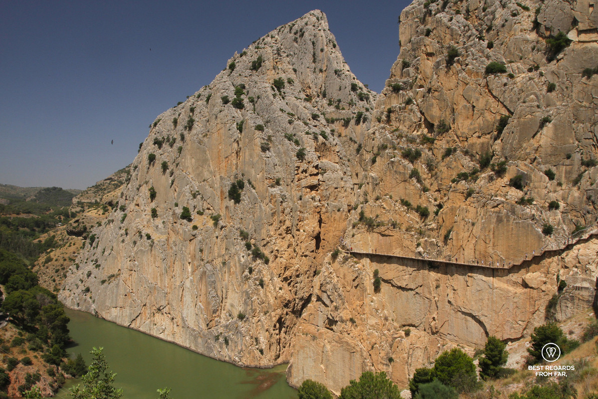 Vertical rocks slabs rising from a lake with the Caminito del Rey boardwalk attached to one side.