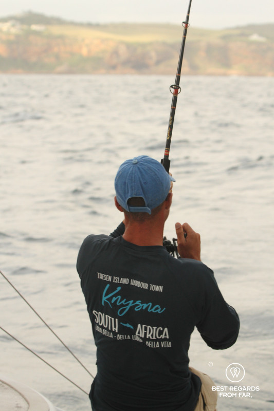 Crew member of Ocean Sailing Charters fishing from the rear of a catamaran.