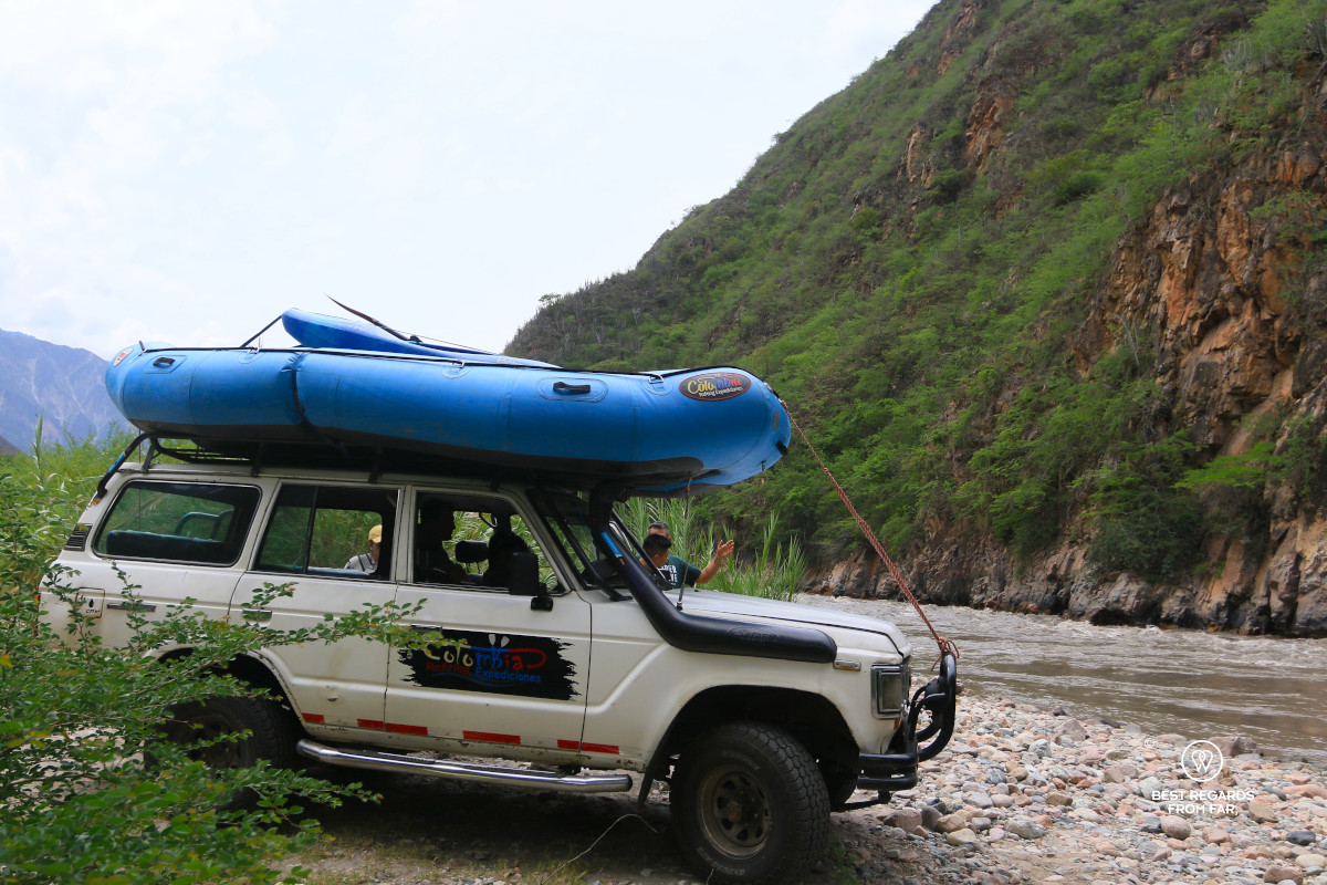4x4 with blue raft on the roof by the river.