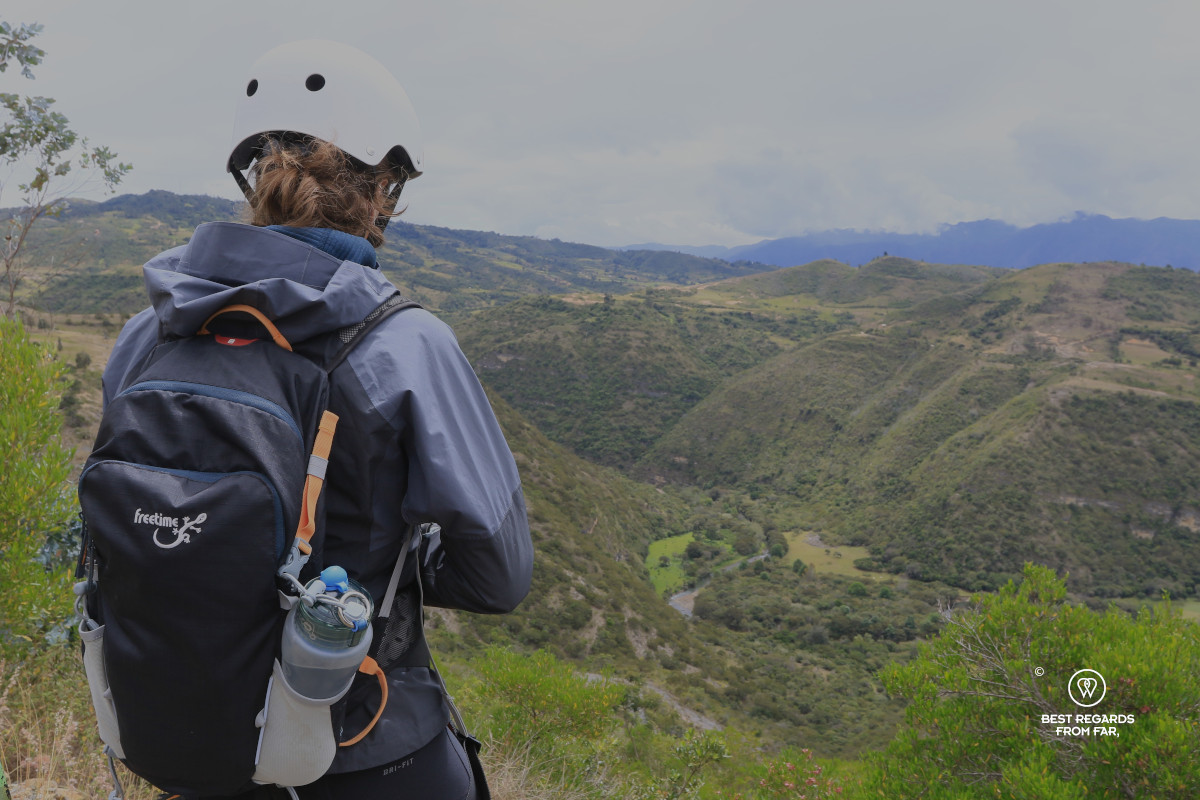 Woman with a Freetime backpack and helmet overlooking a valley before descending into a cave.