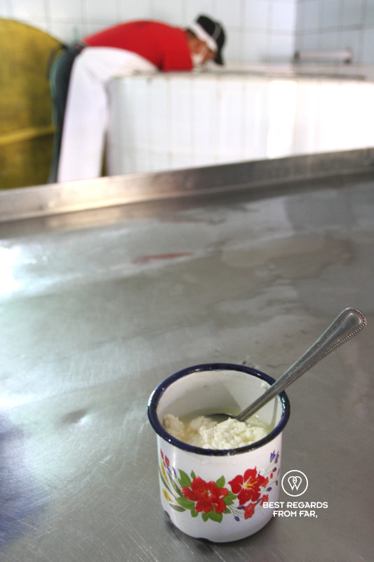 Fresh curd in a cup to be tasted with a man making cheese in the background.