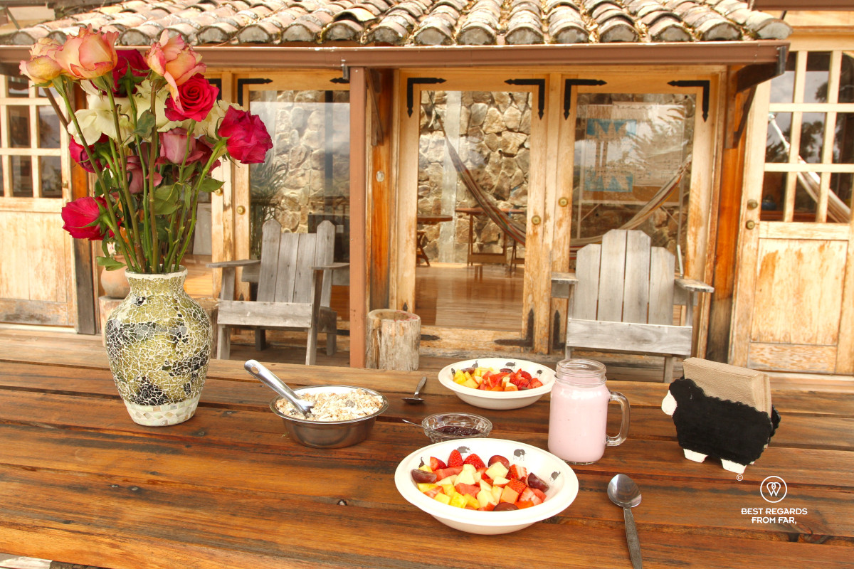 Breakfast with fruits, yogurt and muesli and fresh roses on a wooden table at the Black Sheep Inn in Chugchilan in Ecuador.