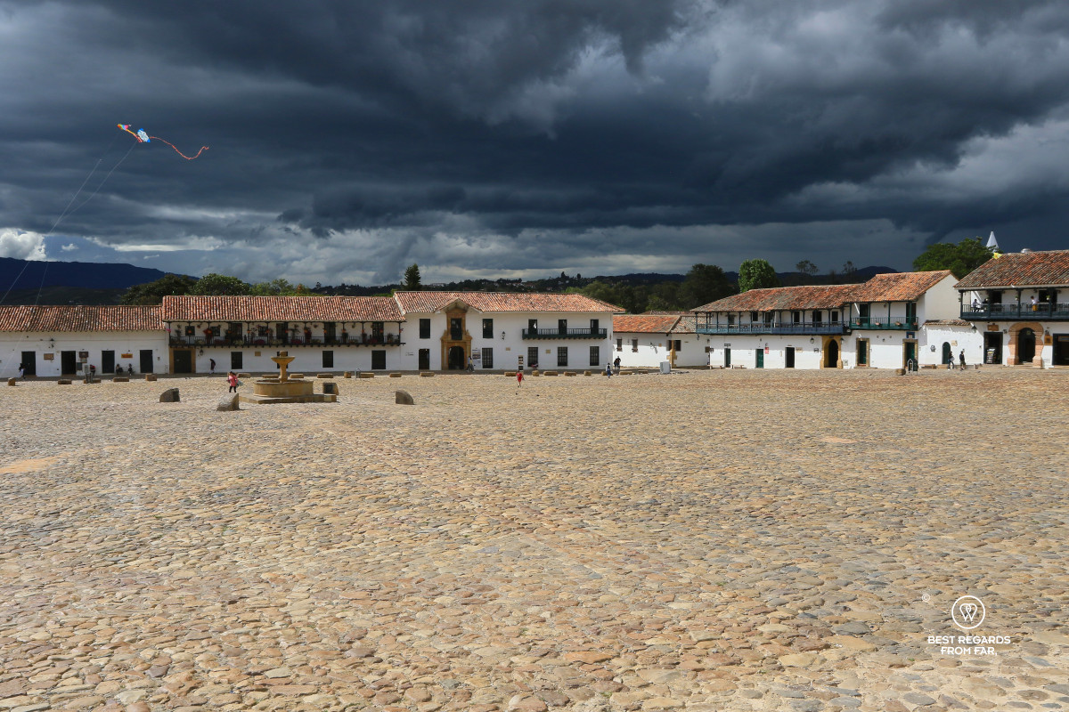 Large cobblestoned square with mountains in the background and dark skies.