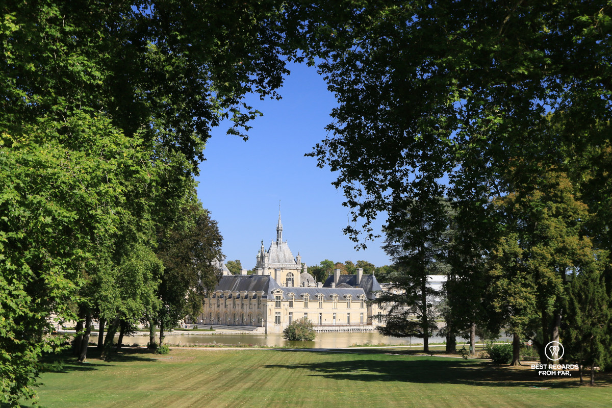 Castle of Chantilly framed by trees and the lawn.