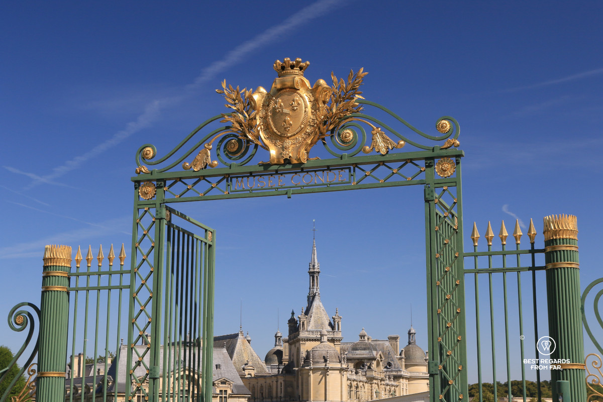The iron gate of the Castle of Chantilly, reading "Musée Condé" with the castle in the background.
