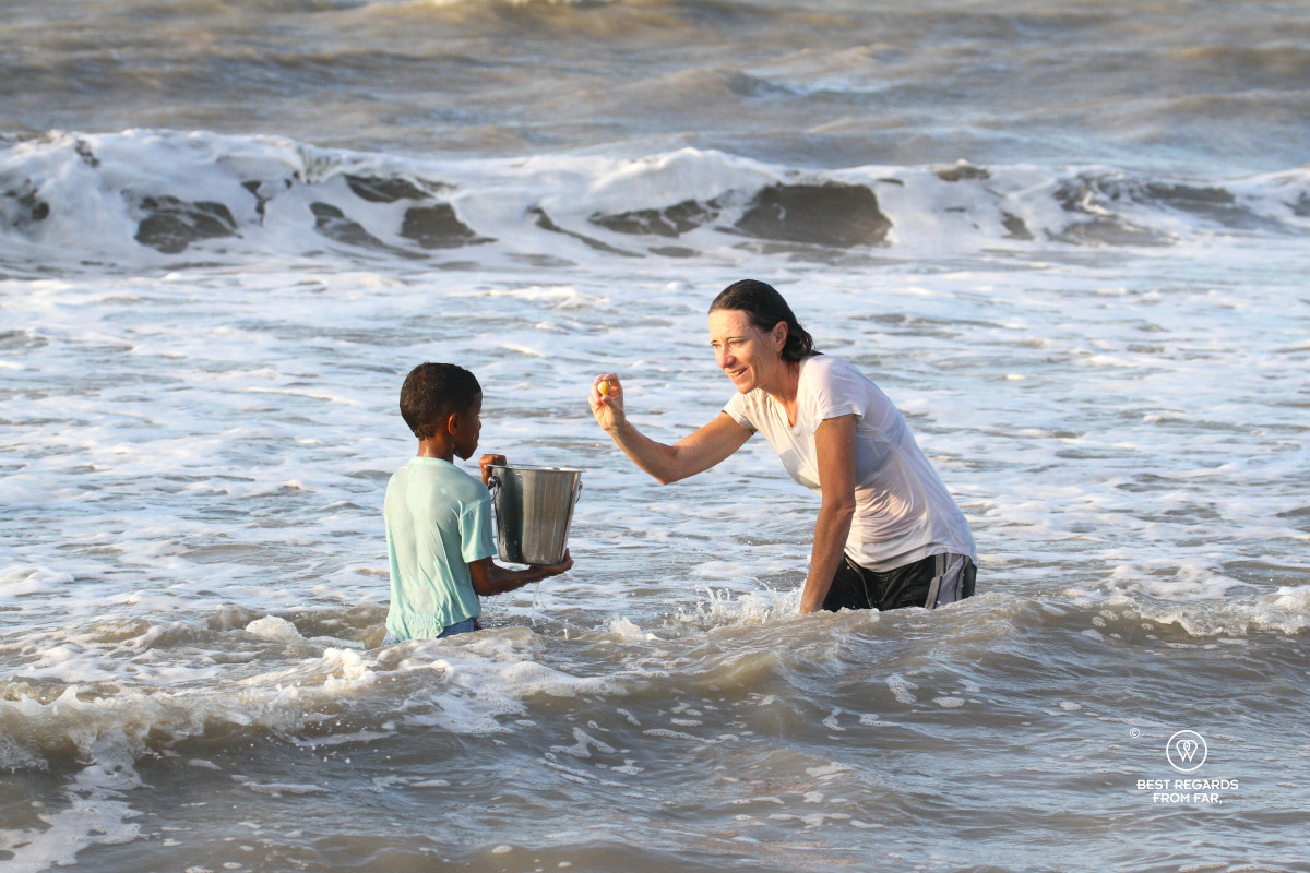 Woman putting a clam in the bucket of a children while they are both in the ocean fishing for clams.