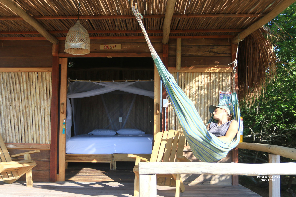 Woman sleeping in a hammock in front of a wooden cabana by the beach.