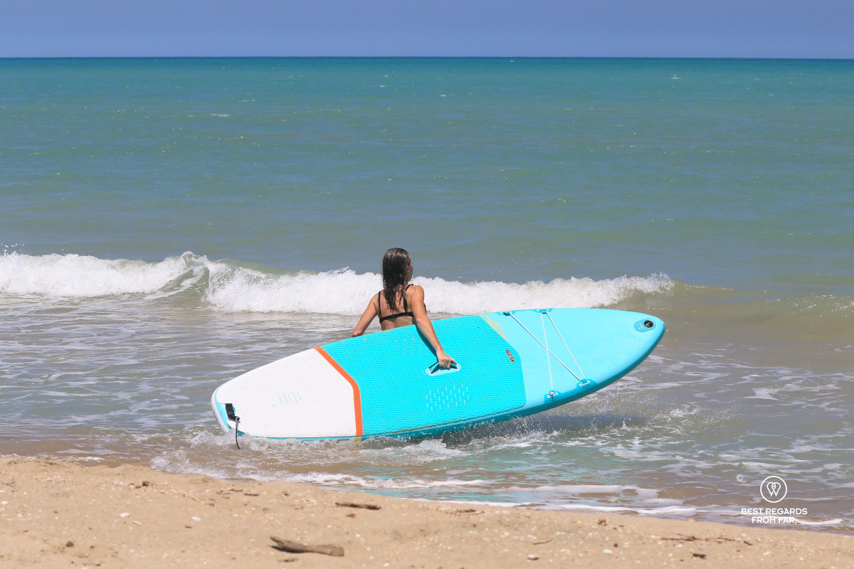Woman entering the blue Caribbean Sea with a white and blue Stand Up Paddleboard.
