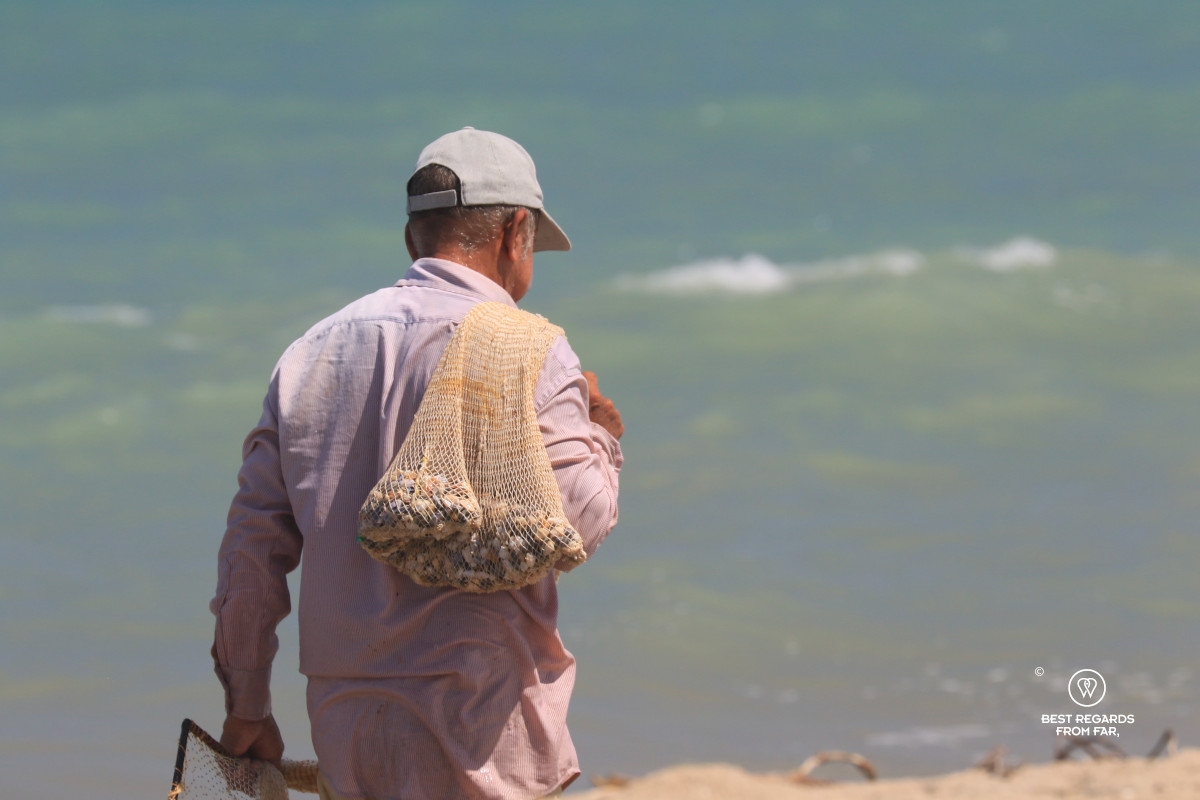 Fisherman walking on the beach with a net full of tellins.