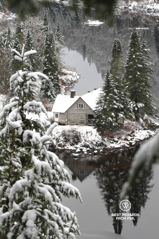 Reflections of fir trees and a chalet covered in snow in the Jacques Cartier River in Quebec.