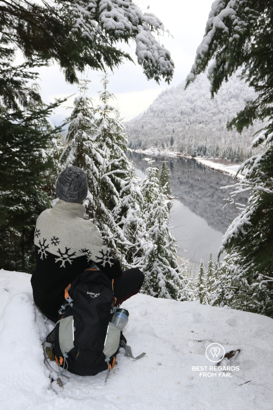 Hiker looking at fir trees covered in snow and the Jacques Cartier River in Quebec.