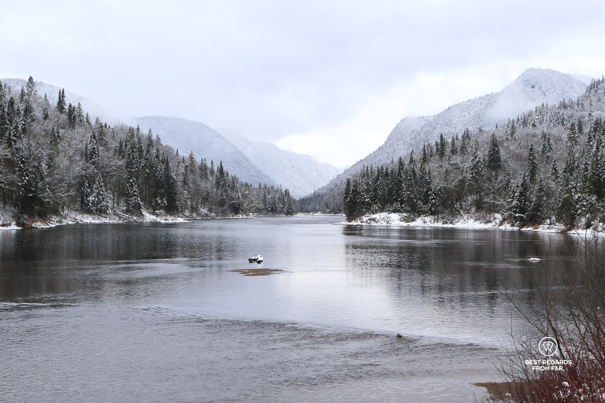 The Jacques Cartier River with fir trees covered in snow and layers of mountains in Quebec.