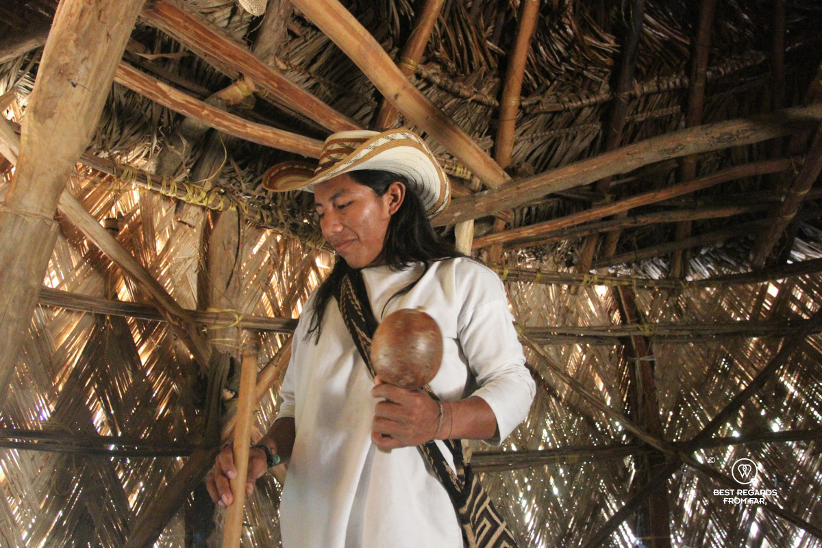 Wiwa man dressed in white in a traditional hut holding his poporo.