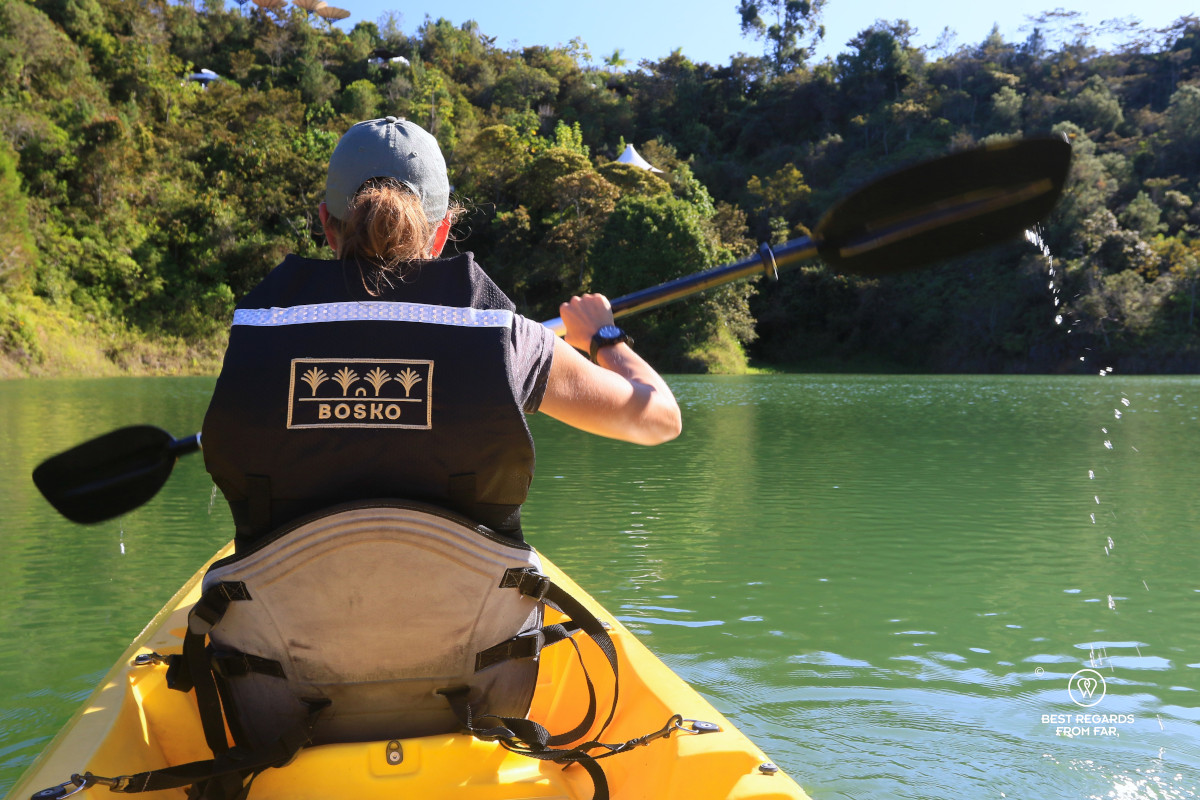 Woman canoeing with a Bosko life jacket on lake Guatape in Colombia with the hotel suites in the background.