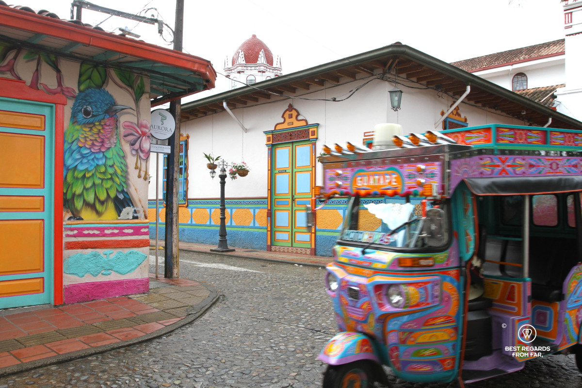 Colorful tuk-tuk rushing by the colorful main square of Guatape.