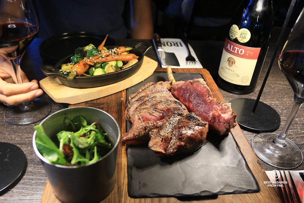 Table with veggies, salad, red wine and a rib eye at Iron Steak and Bar, Cape Town.