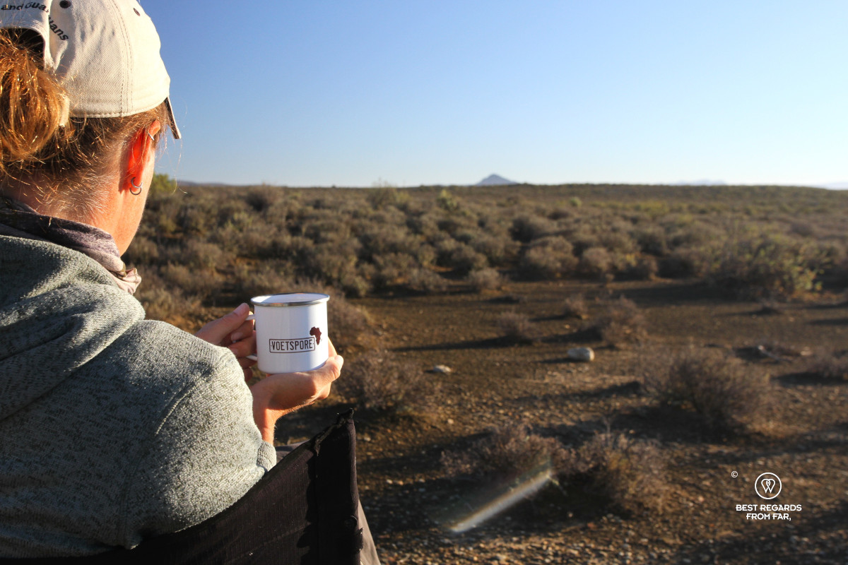 Woman holding a white coffee mug while overlooking a barren landscape.