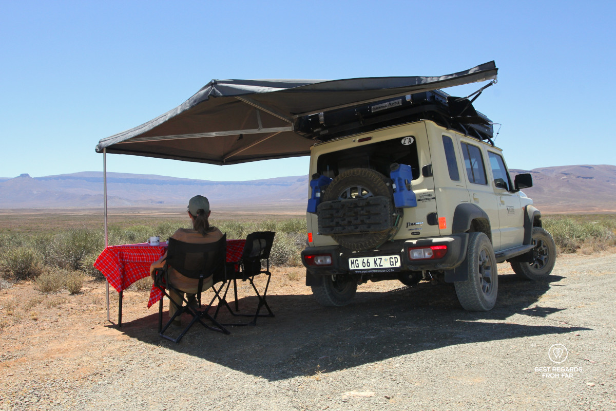 Woman seated in the shade of an ostrich wing attached to a Suzuki Jimny.
