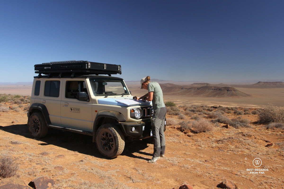 Woman studying the map on the bonnet of a 4x4 to define the route in a barrren landscape.