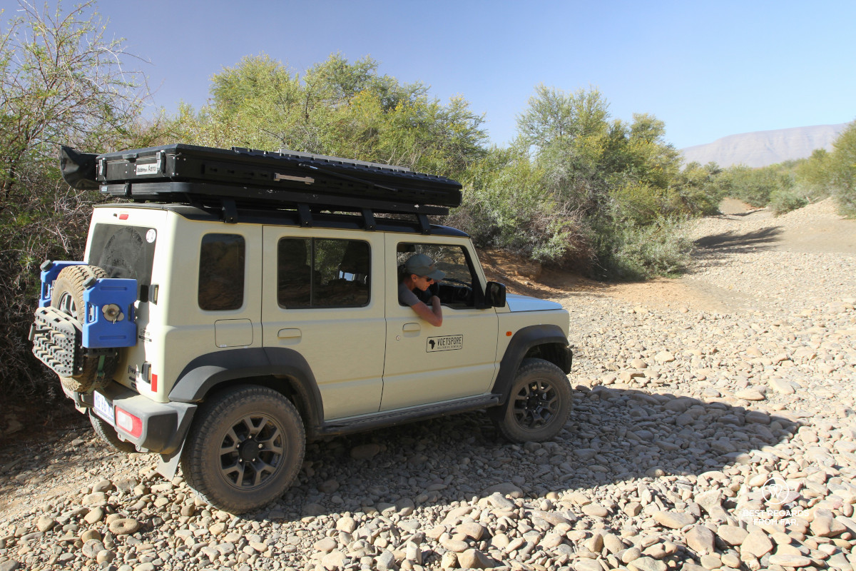 Woman driving a 4x4 through a rocky dry riverbed.