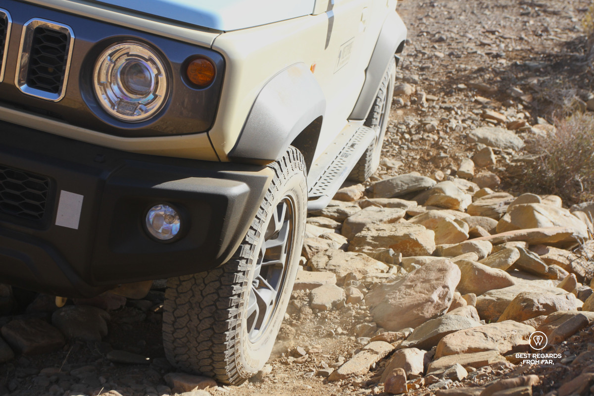 Suzuki Jimny seen from low by the ground with the wheels on the rocks.