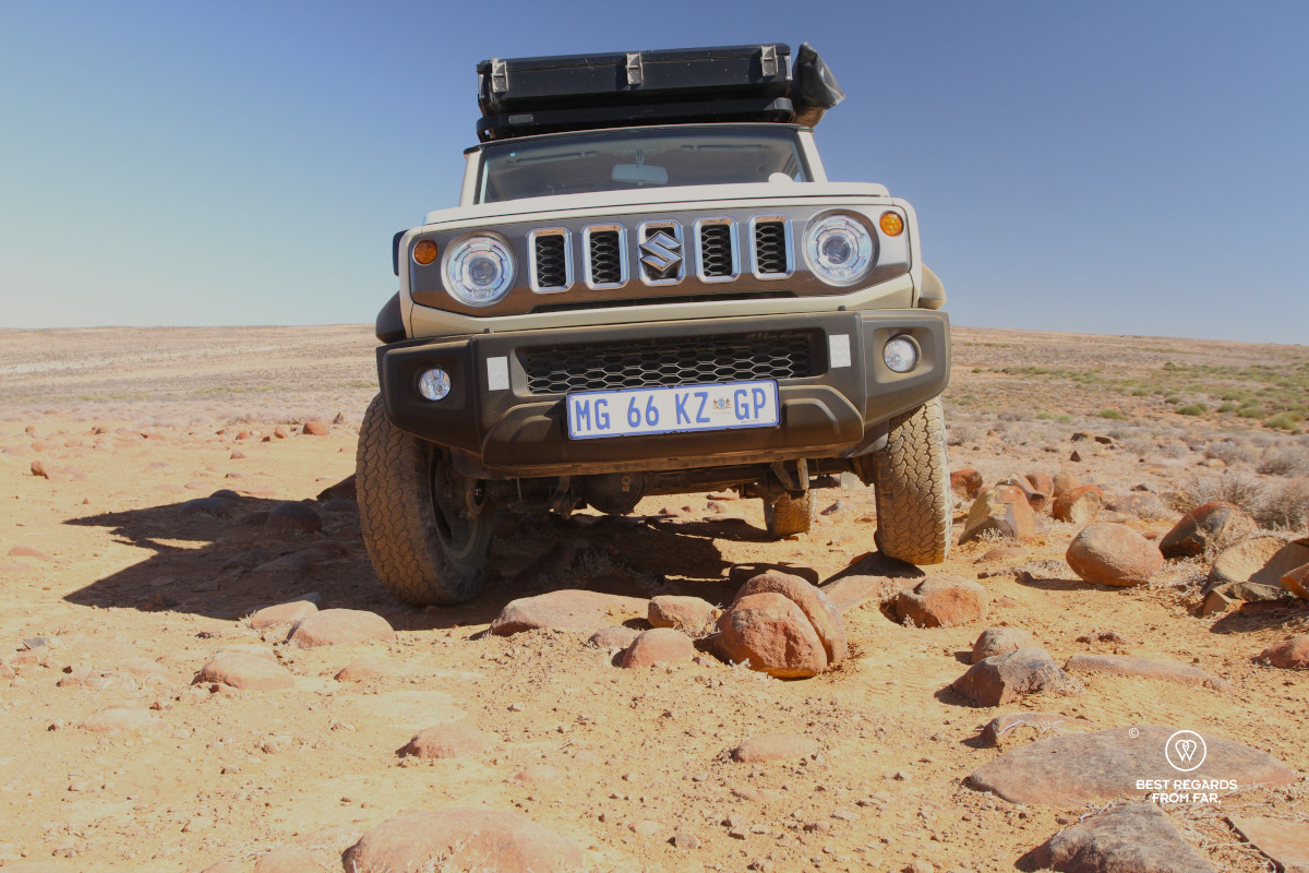 Suzuki Jimny seen from low by the ground with the wheels on the rocks.