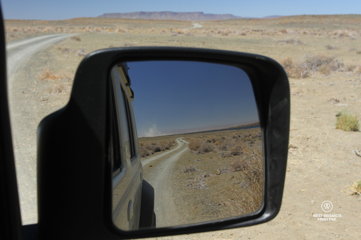 Close-up with focus on a gravel road in the mirror of a car.