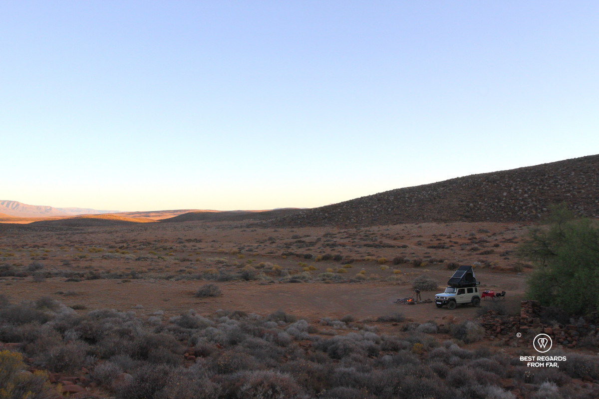 Camp set-up with a Suzuki Jimny, rooftop tent, set table and a fire running at sunset.