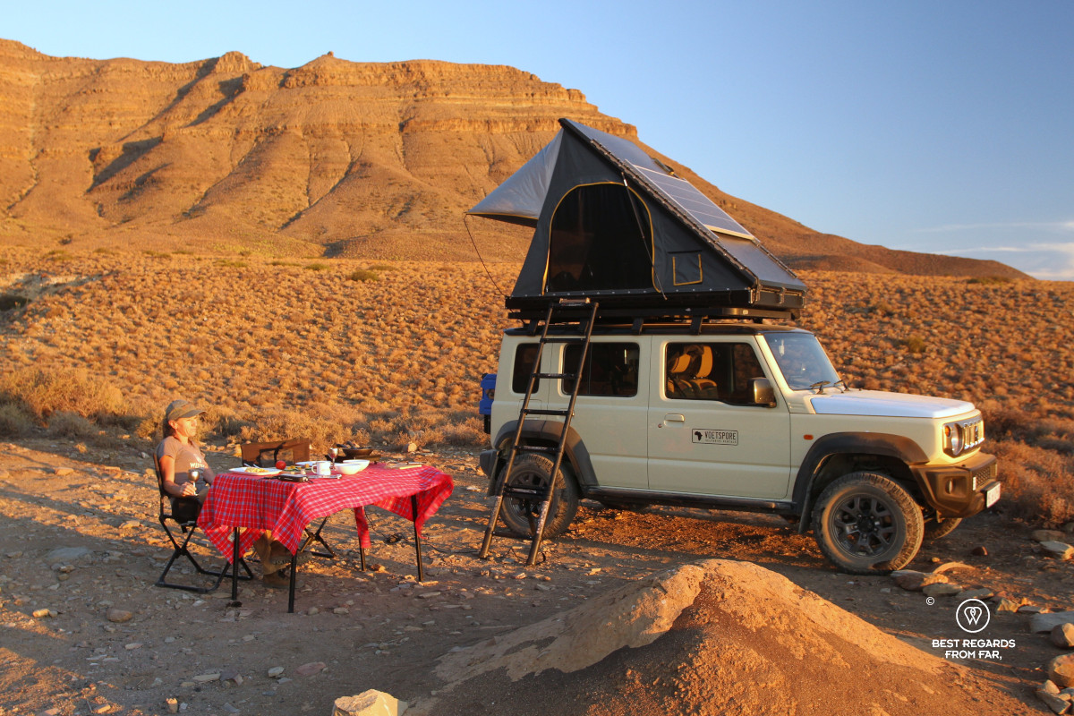 Woman enjoying sunset next to her 4x4 with a rooftop tent.
