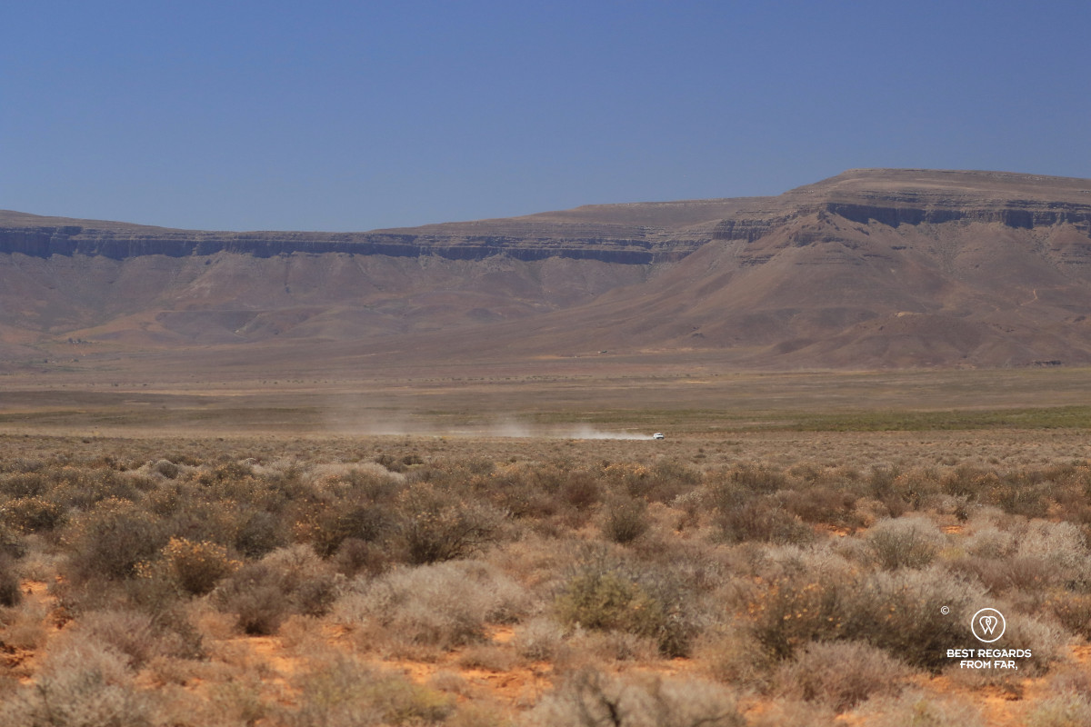 White 4x4 in motion through in the vast landscape of the Tankwa Karoo leaving a trail of dust behind.