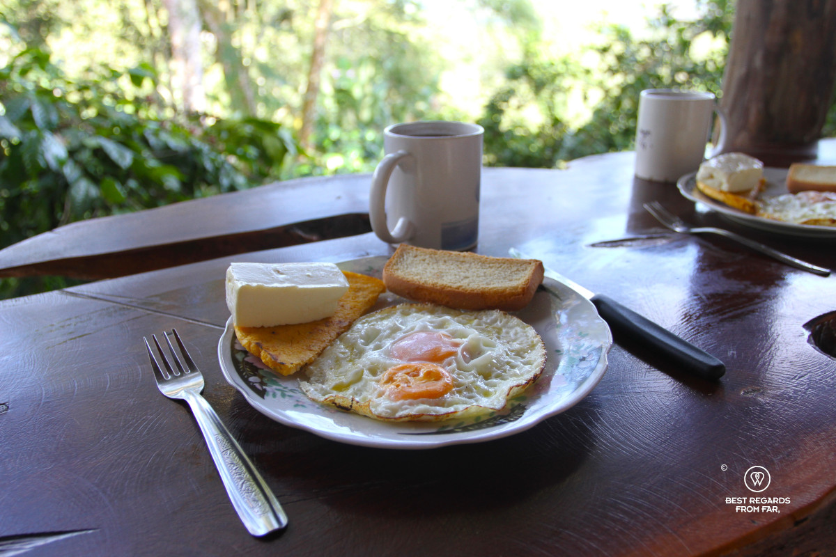 Fried eggs with plantain and cheese and coffee mug on a wooden table by coffee plantation.
