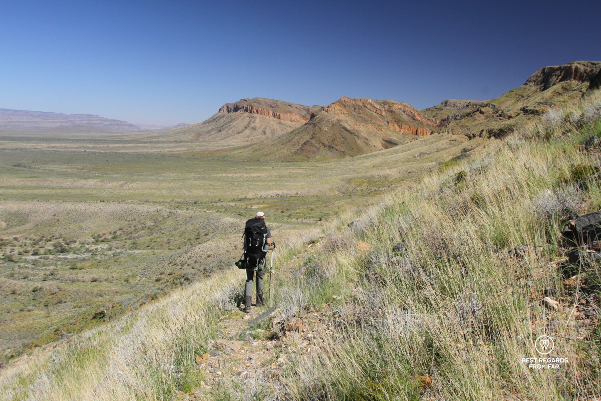 Woman walking on a green mountain slope in the sun.
