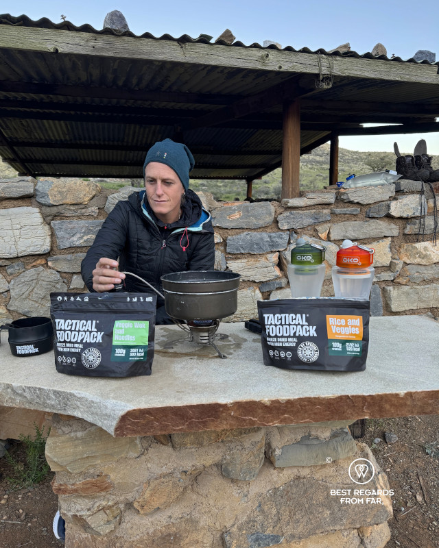 Author Marcella van Alphen warming up water on a stove by a shelter in the outdoors.