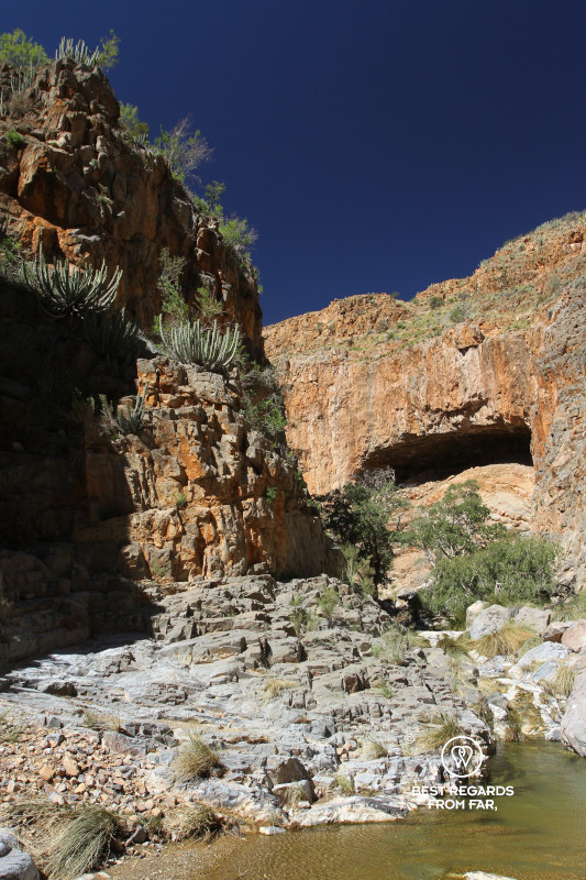 Red canyon with a large cave opening and a rock pool.