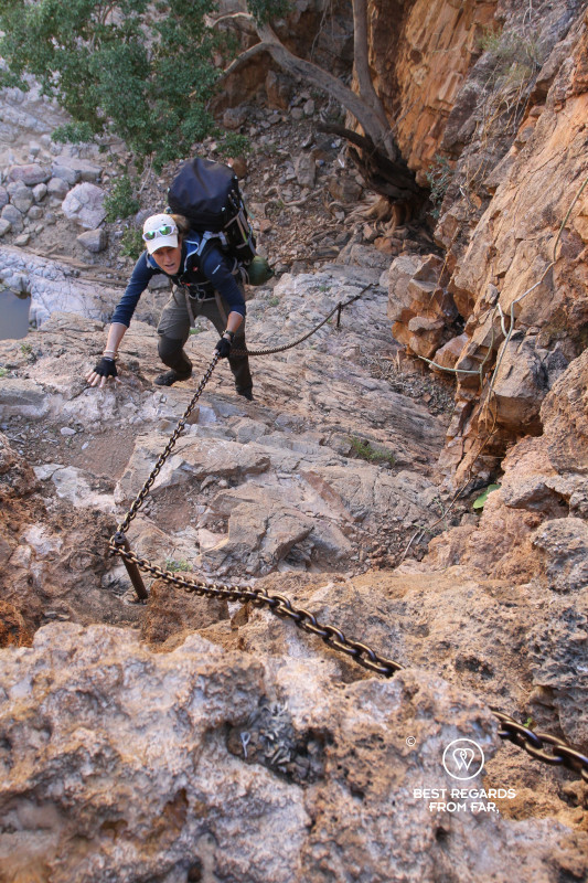 Author Marcella van Alphen making use of a metal chain to climb a steep part along the Naukluft Trail along red rocks.