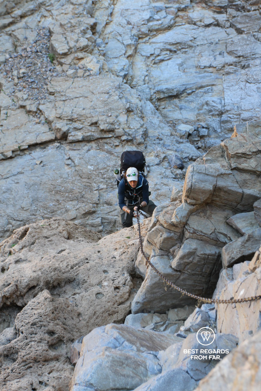 Woman climbing along a rock with the help of a chain.