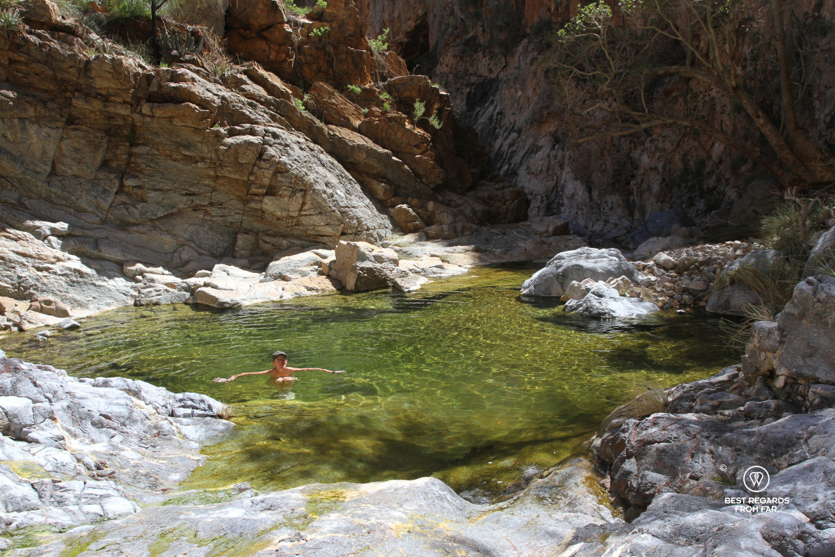 Author Claire Lessiau cooling down in a sun-lit rock pool in a deep canyon.
